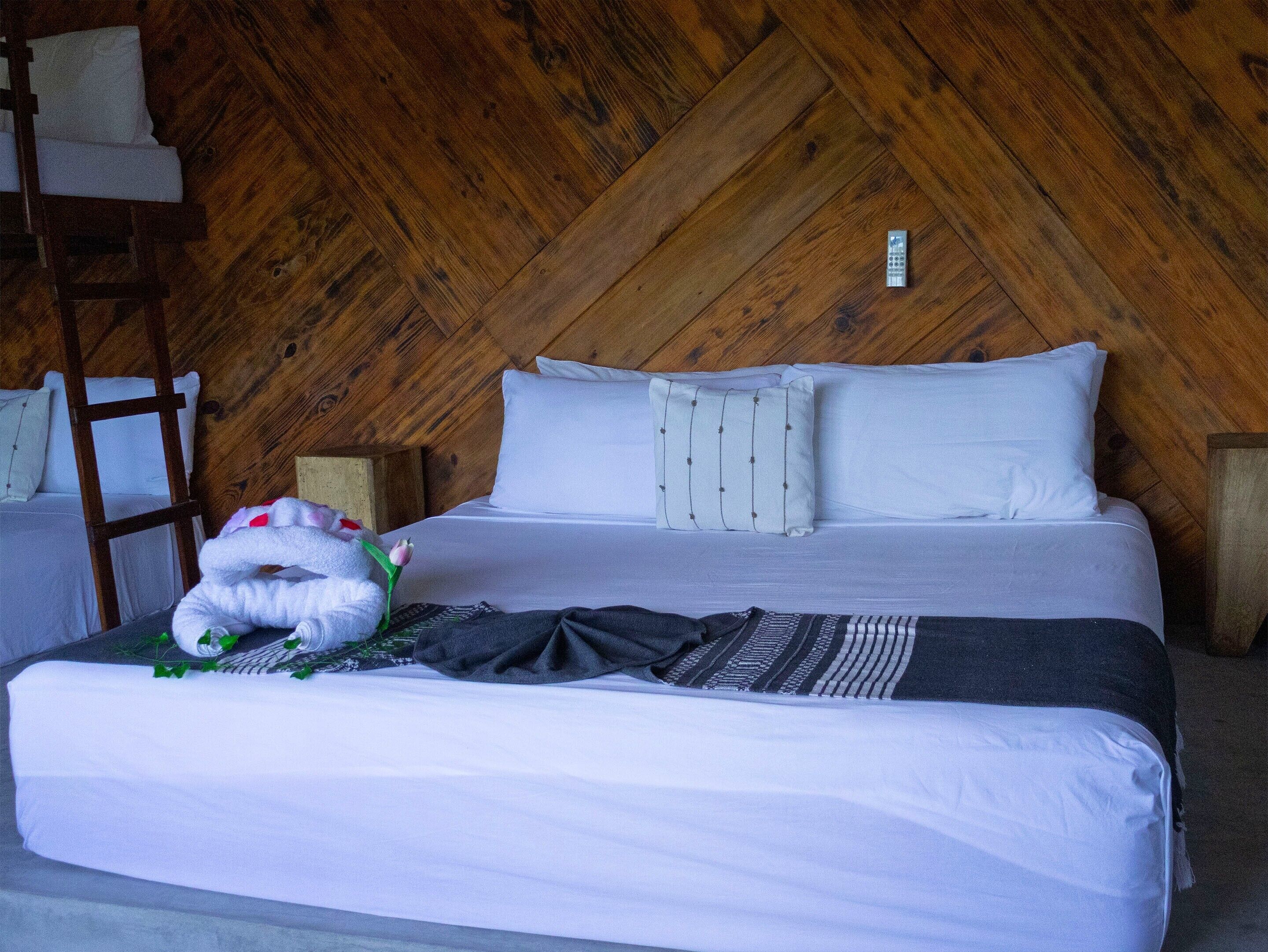 A single bed with white bedding and a decorative pillow, a wooden ladder, and a wooden wall with a herringbone pattern.