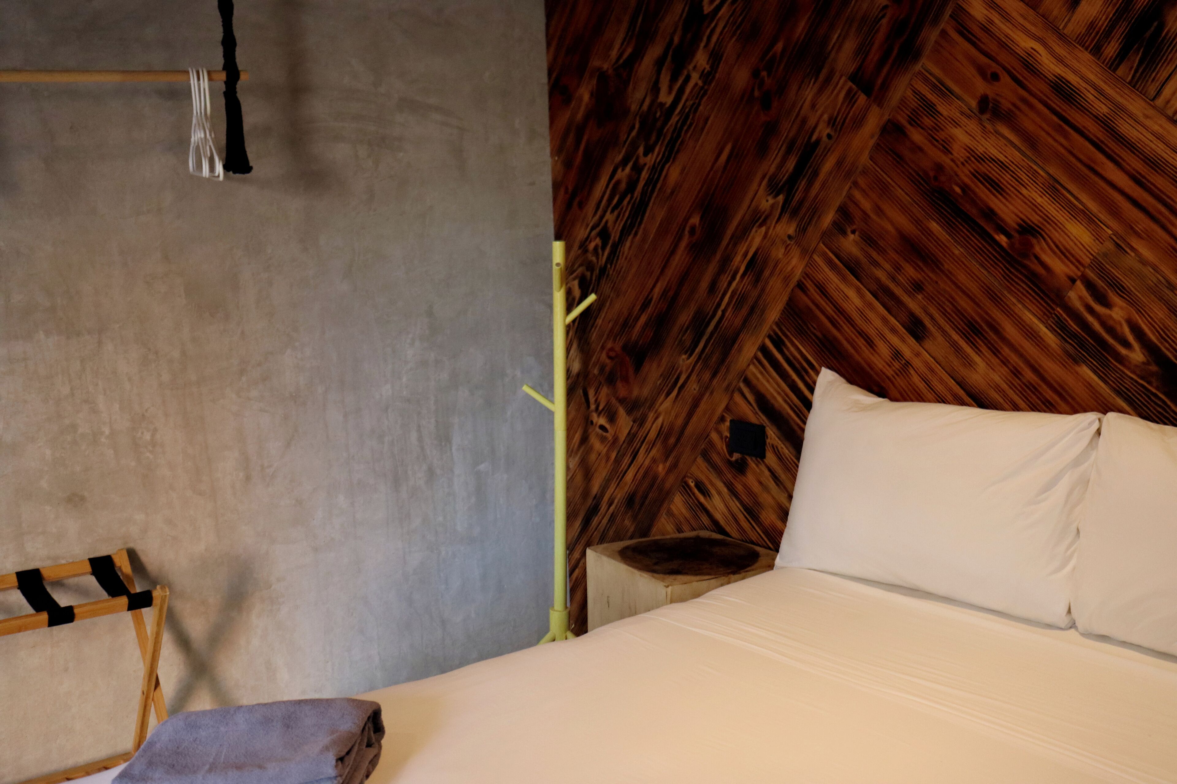 Una cama con sábanas blancas, cabecera de madera y pared gris.