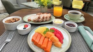 Un desayuno con una fuente de fruta cortada, un vaso de zumo de naranja y una taza de café.