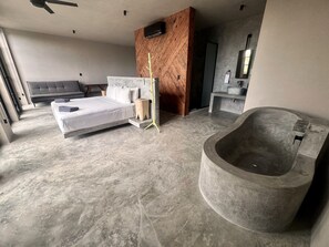 Une chambre moderne avec un grand lit, un mur d’accent en bois, une salle de bain avec baignoire et un sol en marbre gris.