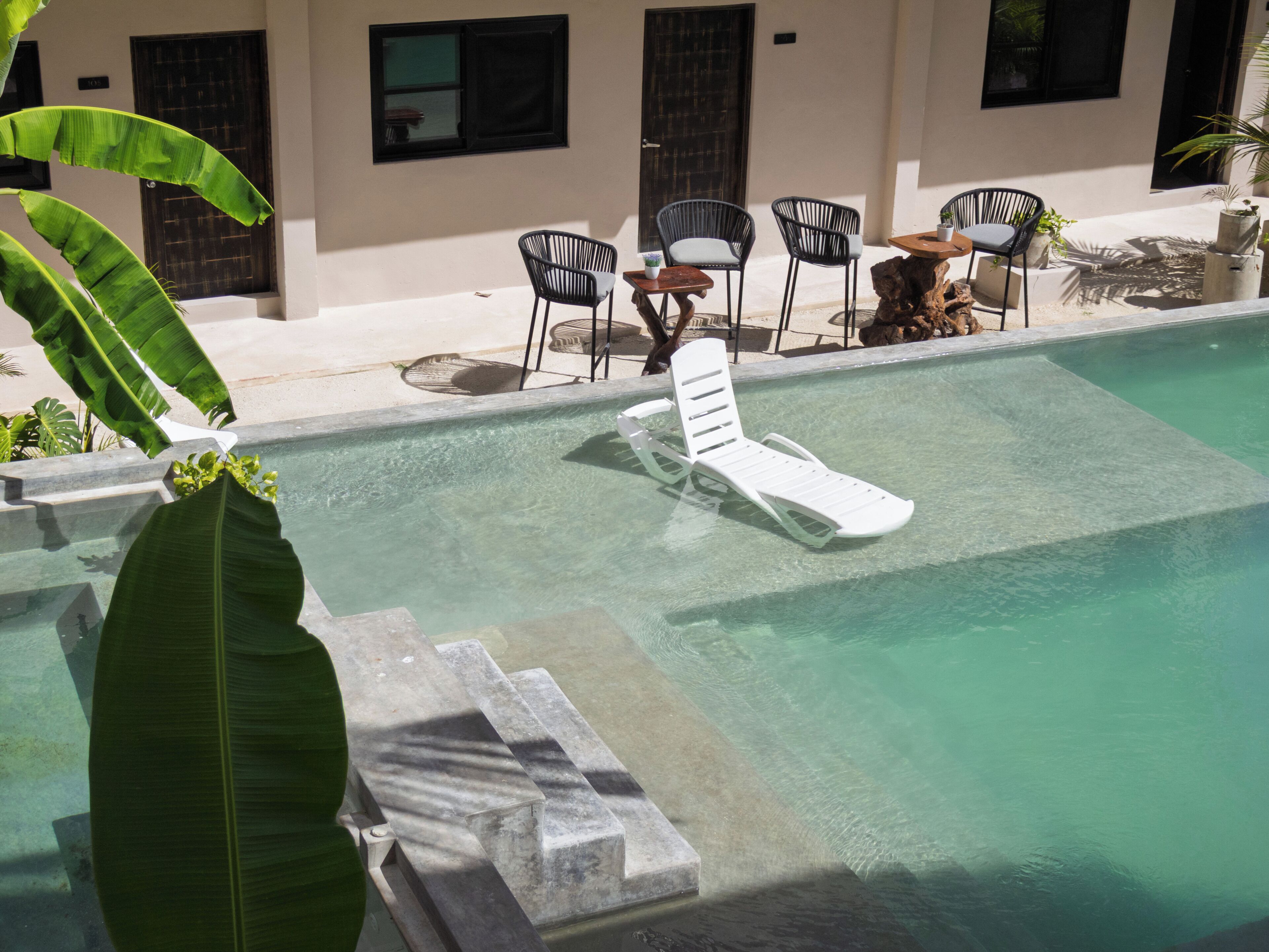Une piscine avec des chaises longues, des chaises et des plantes en pot.