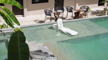 Une piscine avec des chaises longues, des chaises et des plantes en pot.