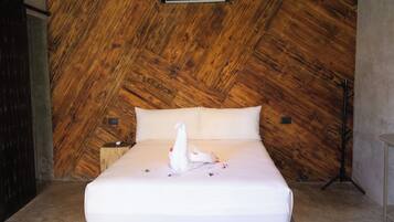 A bed with white linens, a white towel, and a decorative swan in a room with wooden paneling and a wall-mounted air conditioning unit.