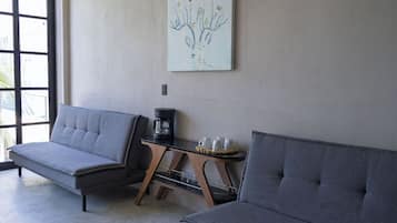 Una habitación con dos sofás grises, una cafetera y una mesita con tazas y una bandeja.