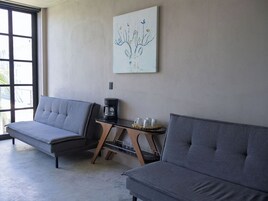 Una habitación con dos sofás grises, una cafetera y una mesita con tazas y una bandeja.