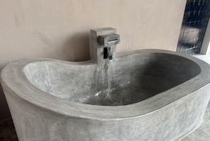 Ein großer, rechteckiger Steinwaschbecken mit einem Wasserhahn, aus dem Wasser fließt, und einer strukturierten Wand im Hintergrund.