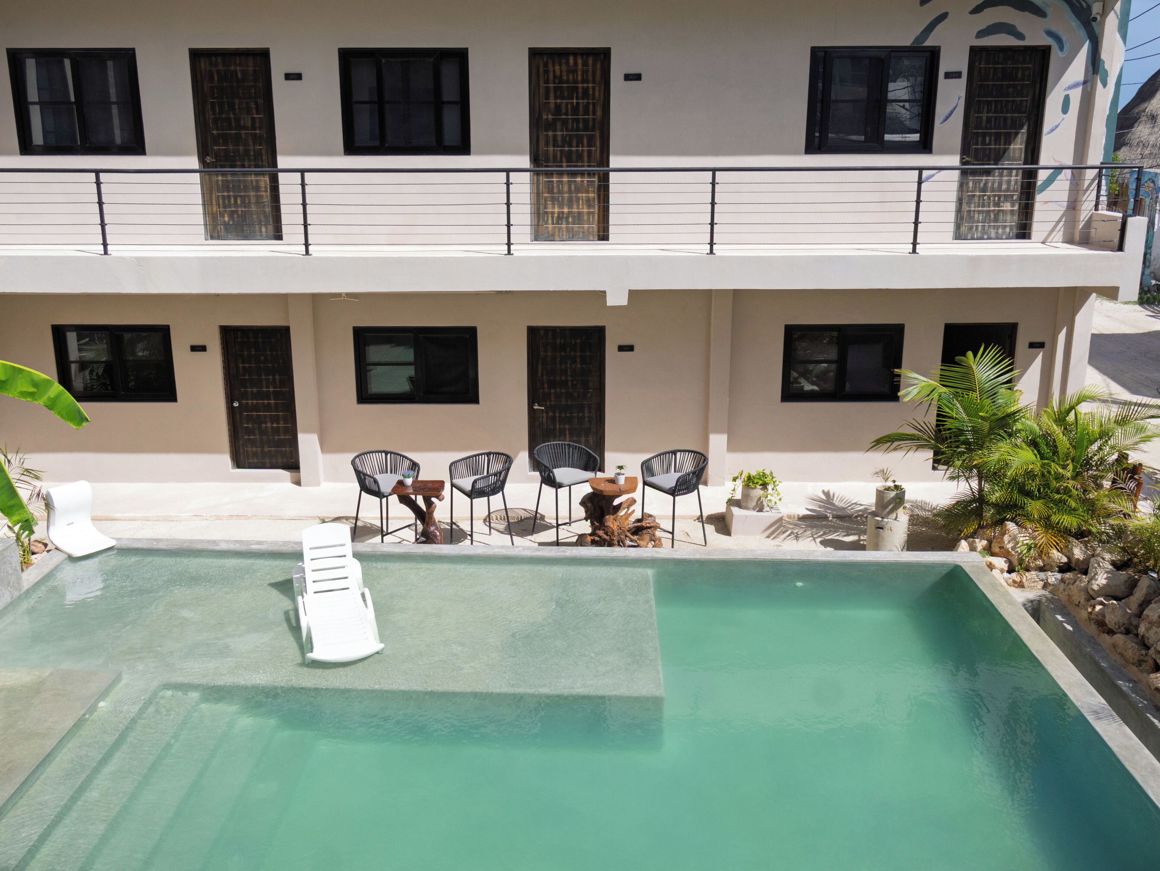 A swimming pool with lounge chairs and a small table, surrounded by a building with multiple windows and doors.