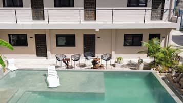 A swimming pool with lounge chairs and a small table, surrounded by a building with multiple windows and doors.