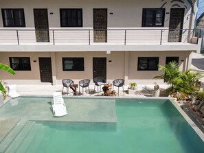 Una piscina con sillones de descanso y una pequeña mesa, rodeada por un edificio con varias ventanas y puertas.