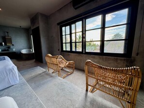 A modern room with a large window, a bed, a bathroom, and two wicker chairs. - Piscis Art by ÓOL Hotels (Isla Holbox)