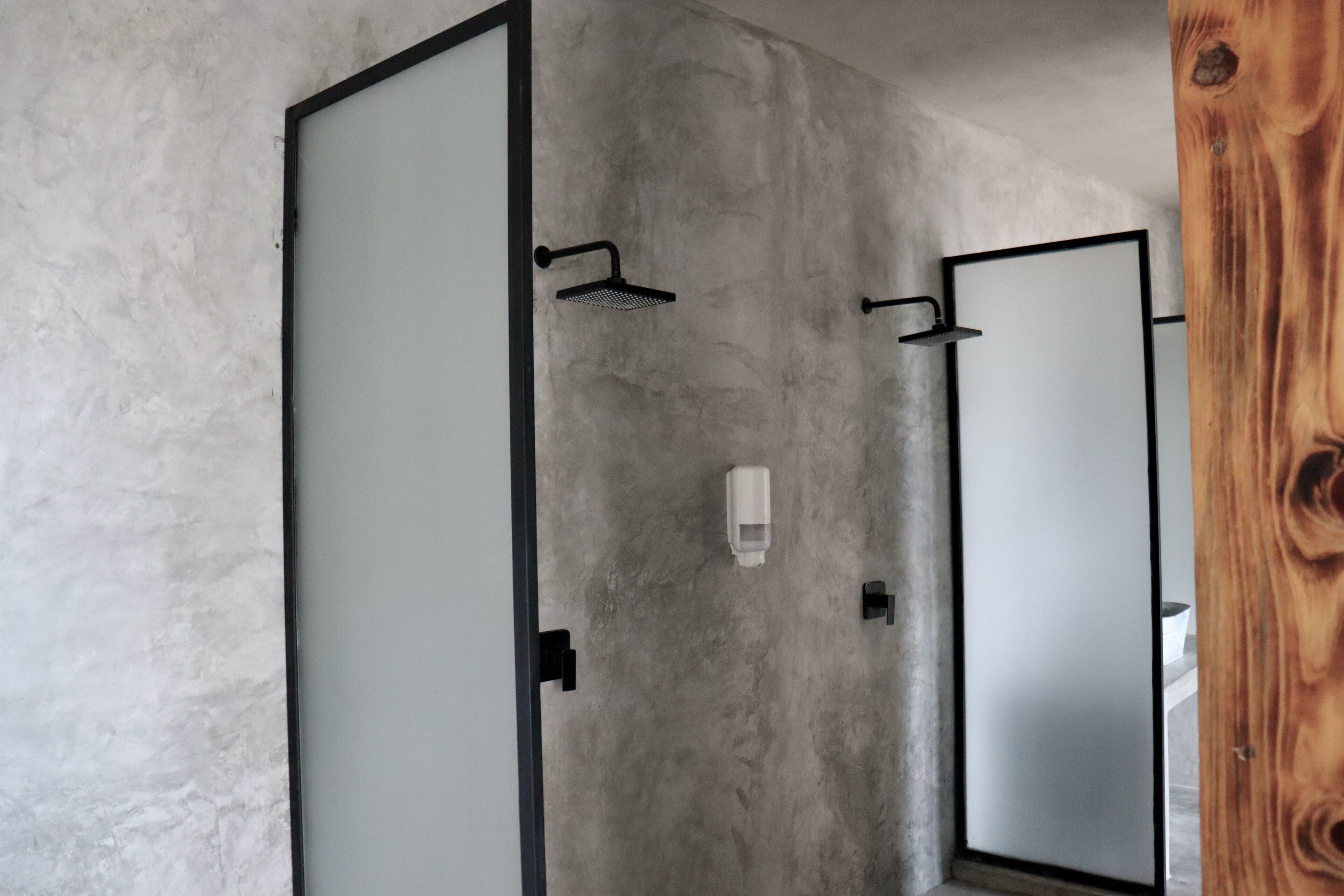Un baño con pared de concreto, un marco de puerta de madera y un espejo.