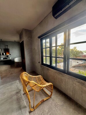 A modern interior with a large window, a wicker chair, and a concrete floor. - Piscis Art by ÓOL Hotels (Isla Holbox)
