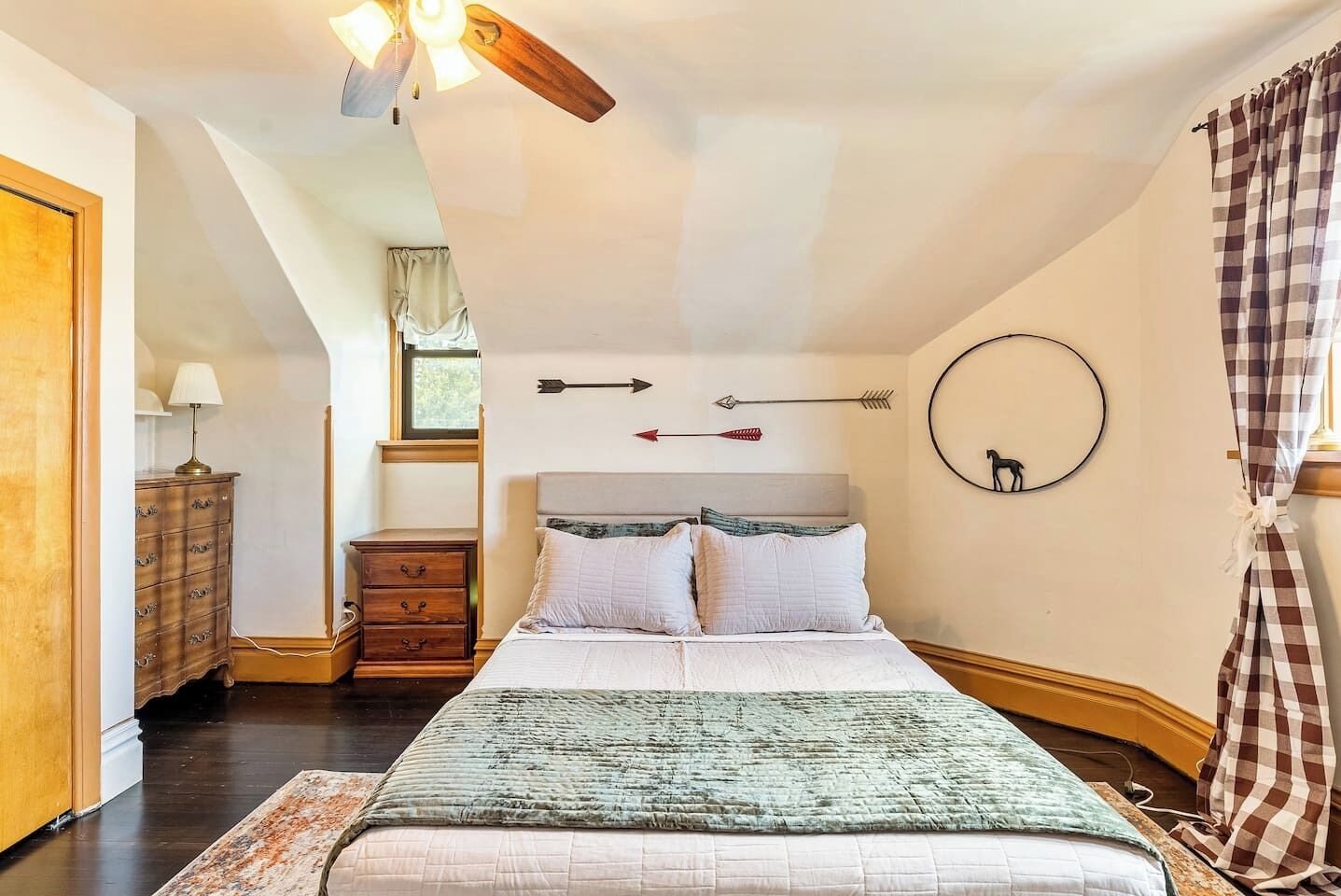 A bedroom with a bed, a dresser, a lamp, and a ceiling fan.