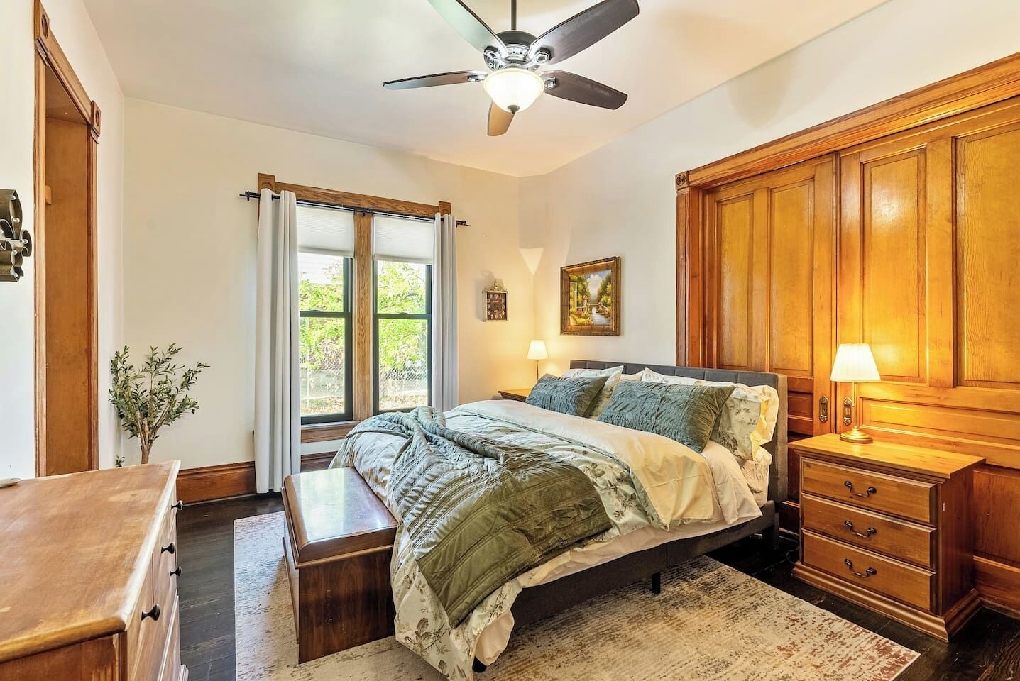 Ein Schlafzimmer mit einem Bett, Nachttischen, einem Deckenventilator, einem Fenster mit Vorhängen und einem Holzschrank.
