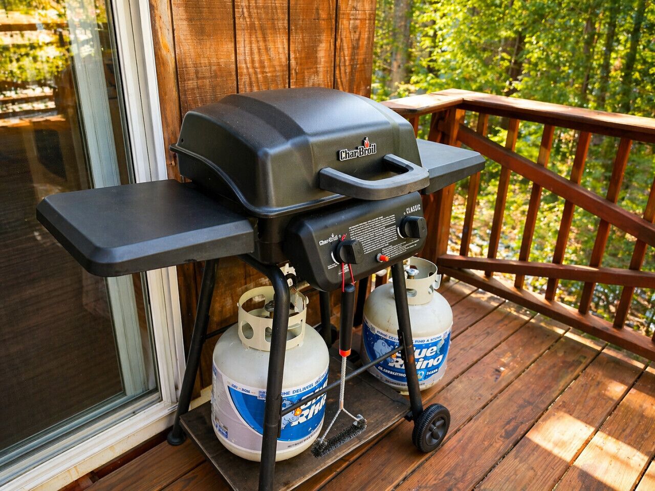 A Char-Broil grill on a wooden deck with propane tanks.