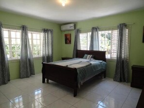 A bedroom with a bed, curtains, an air conditioning unit, and a tiled floor. - Beach Access, 1 Bed 1 Bath in Coral Garden (Montego Bay)