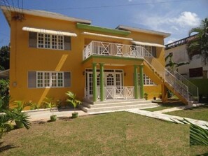 A two-story yellow building with a balcony, a staircase, and a small front yard. - Beach Access, 1 Bed 1 Bath in Coral Garden (Montego Bay)