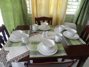 A dining table set with white dishes and cups, a lace table runner, and green-striped placemats. - Beach Access, 1 Bed 1 Bath in Coral Garden (Montego Bay)