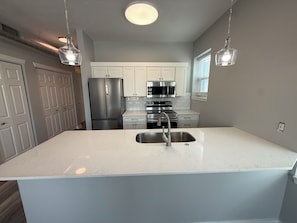 Una cocina con armarios blancos, electrodomésticos de acero inoxidable e iluminación colgante.