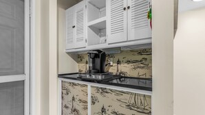 Cozinha com armários brancos, máquina de café e parede com papel de parede de temática náutica.
