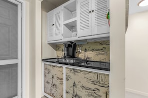 A kitchen with white cabinets, a coffee machine, and a wall with nautical-themed wallpaper. - Cozy Condo Getaway! (Naples)