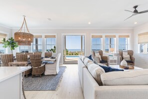 A spacious living area with a large sofa, wicker chairs, a dining table, and a view of the ocean. - Cape San Blas gulf front home with private pool and elevator (Port St. Joe)