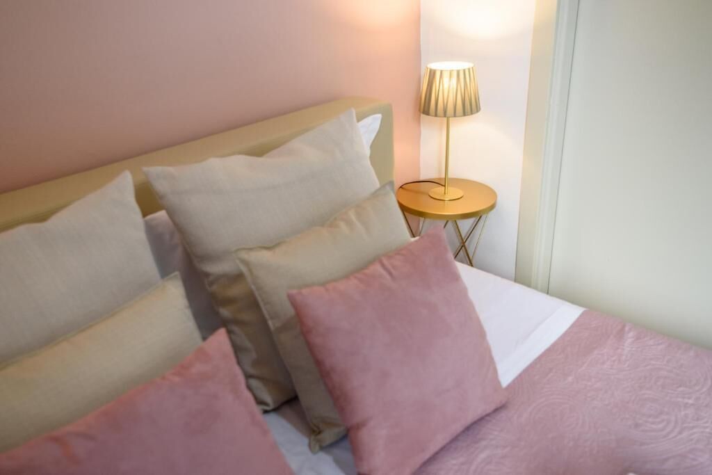 Ein Bett mit vielen Kissen, einer Nachttischlampe und einer Wand mit einer Tür.