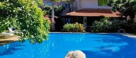 A poolside view with mountains in the background, a wheelchair, and a house with a red roof.