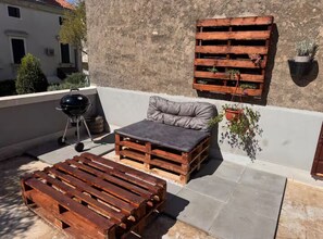 A rooftop terrace with a wooden bench, a cushioned seating area, a barbecue grill, and potted plants. - Apartment old Town-novigrad 20 m From the sea (Novigrad)
