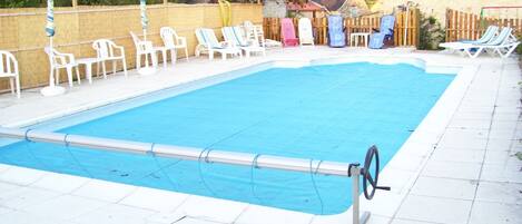 A rectangular swimming pool with a pool ladder, surrounded by white plastic chairs and umbrellas.