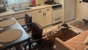 Kompakti keittiö, jossa on liesi, jääkaappi sekä ruokailutila tuoleineen ja pöytineen.