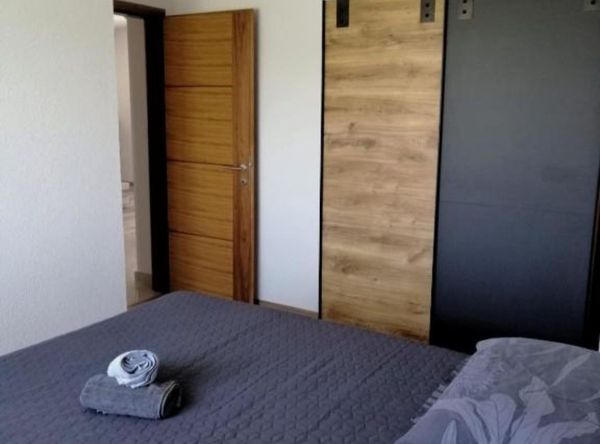 A bedroom with a bed, a wooden wardrobe, and a dark-colored door.