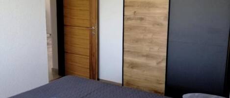 A bedroom with a bed, a wooden wardrobe, and a dark-colored door.