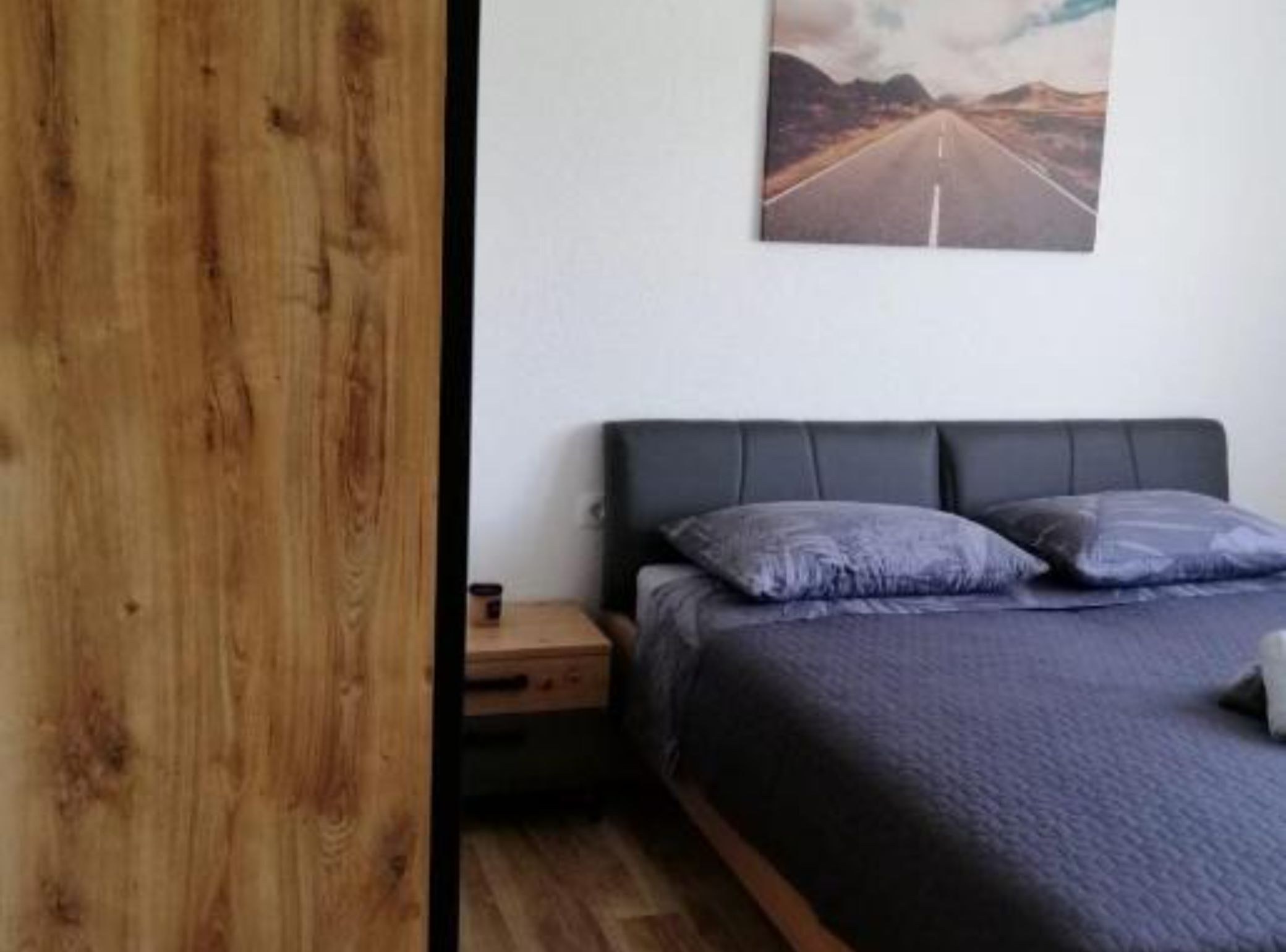Un dormitorio con cama, almohadas, una mesita de noche y un cuadro en la pared.