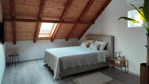 A bedroom with a sloped ceiling, a bed, a small bedside table, a chair, and a potted plant. - Apartment Penthouse Ivan (Drnis)