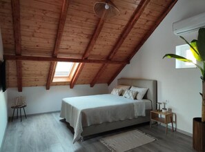 A bedroom with a sloped ceiling, a bed, a small bedside table, a chair, and a large plant. - Apartment Penthouse Ivan (Drnis)