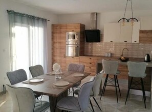 A modern kitchen with a dining area, featuring a wooden table, chairs, and a built-in oven. - Apartment Penthouse Ivan (Drnis)