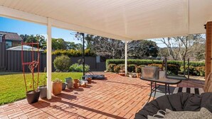 A covered patio with a brick floor, outdoor furniture, potted plants, and a swing set.