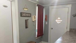 A room with a bench, a wall-mounted sign reading 'LAKE HOUSE,' a telephone, and a window with red curtains. - Ellis Kansas Lakehouse (Ellis)