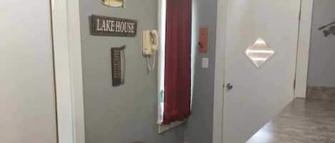 A room with a bench, a wall-mounted sign reading 'LAKE HOUSE,' a telephone, and a window with red curtains.