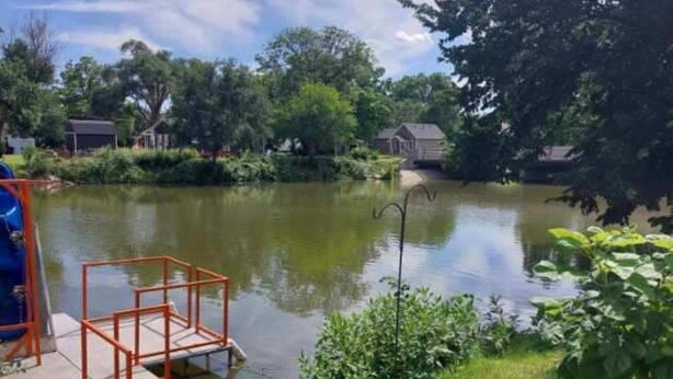 A lakeside area with a dock, grassy banks, and trees. - Ellis Kansas Lakehouse (Ellis)