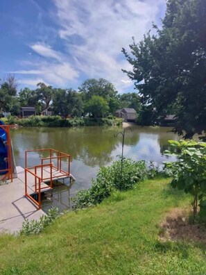 A lakeside area with a dock, grassy banks, and trees. - Ellis Kansas Lakehouse (Ellis)