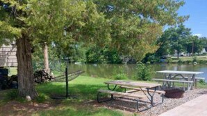 A picnic area with a table and benches, surrounded by grass and trees, near a body of water. - Ellis Kansas Lakehouse (Ellis)