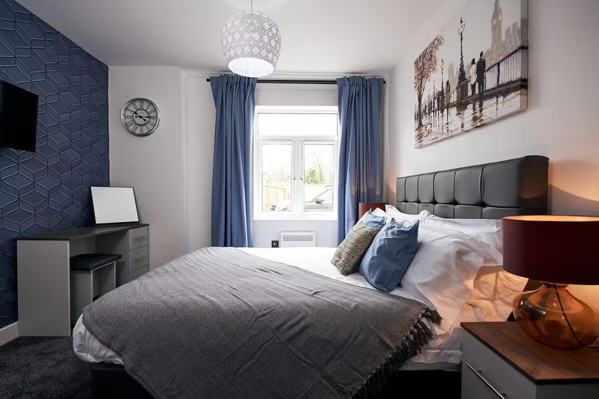 A modern bedroom with a bed, bedside table, lamp, and a window with curtains.