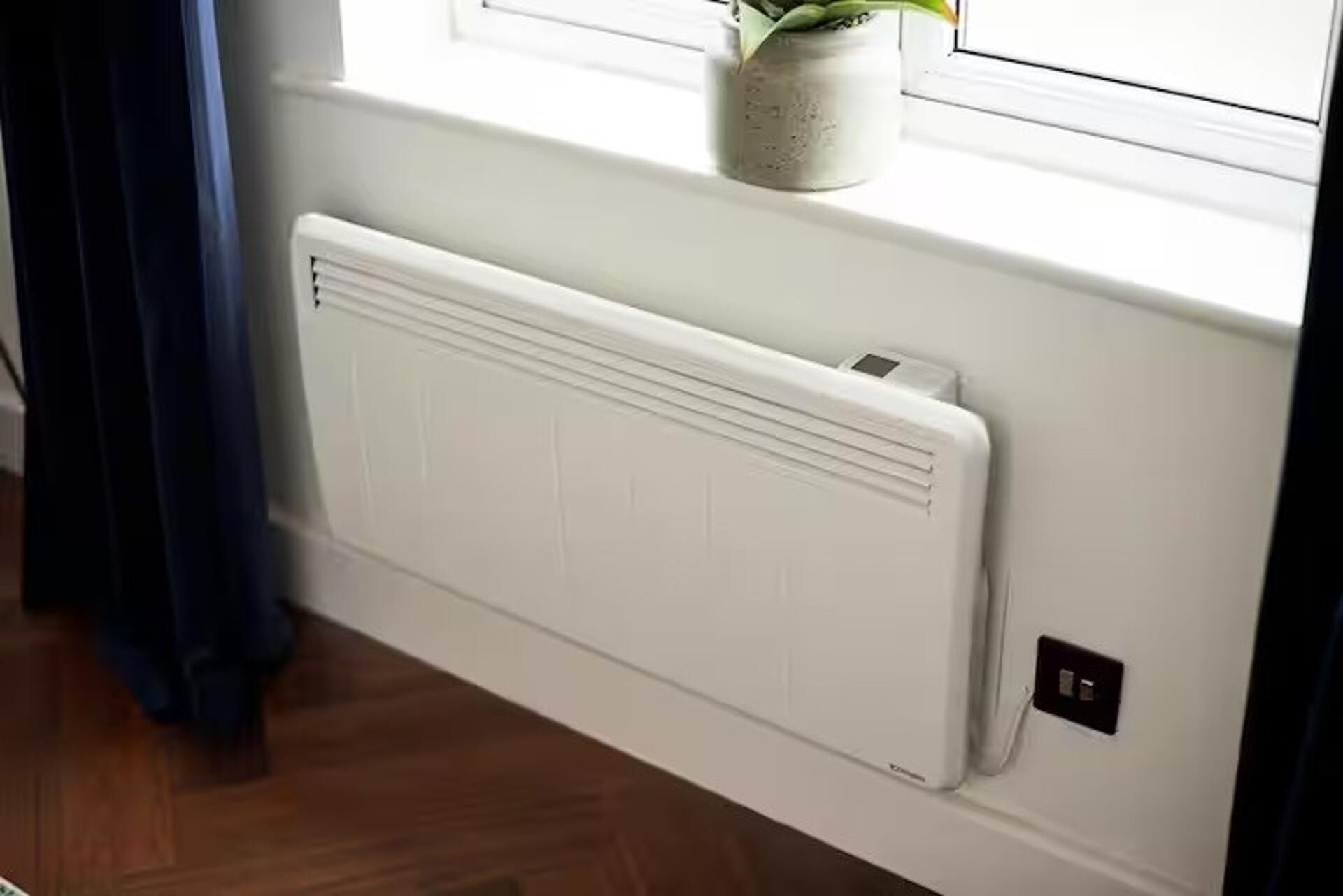 A white radiator on a wall near a window with a potted plant on the sill.