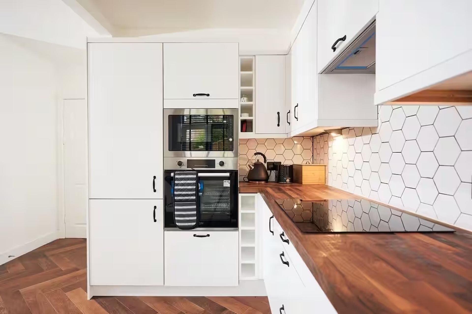 Una cocina moderna con armarios blancos, horno empotrado y encimera de madera.