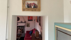 A room with a wooden-framed picture of chickens, a red sofa, a bookshelf, and a lamp. - Apartment in the midst of nature that will help regenerate your body and mind (Castiglione dei Pepoli)
