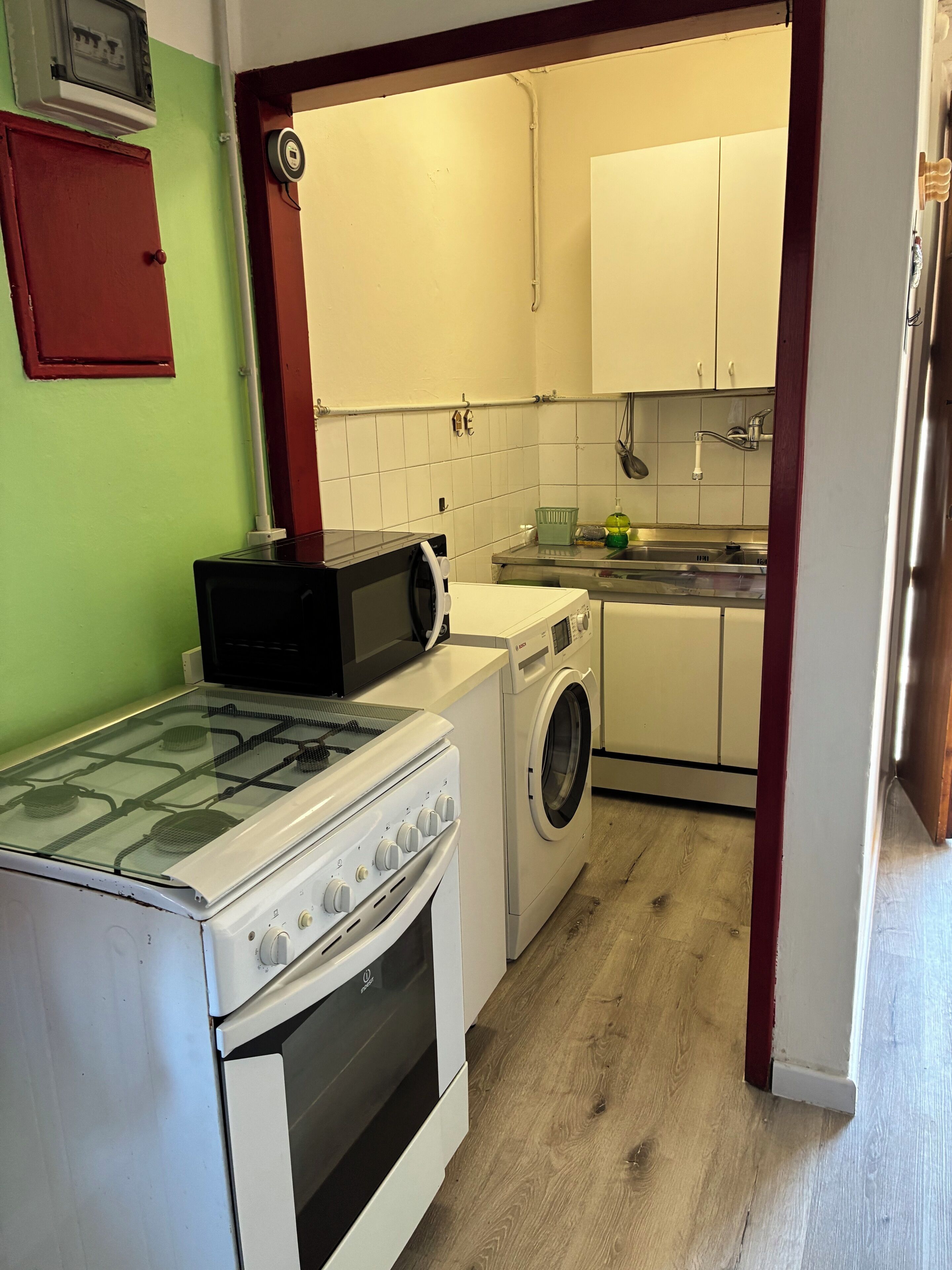 A compact kitchen with a gas stove, microwave, washing machine, and a small sink.
