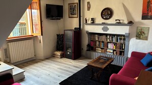 A living room with a TV, bookshelf, red sofa, and a fireplace. - Apartment in the midst of nature that will help regenerate your body and mind (Castiglione dei Pepoli)