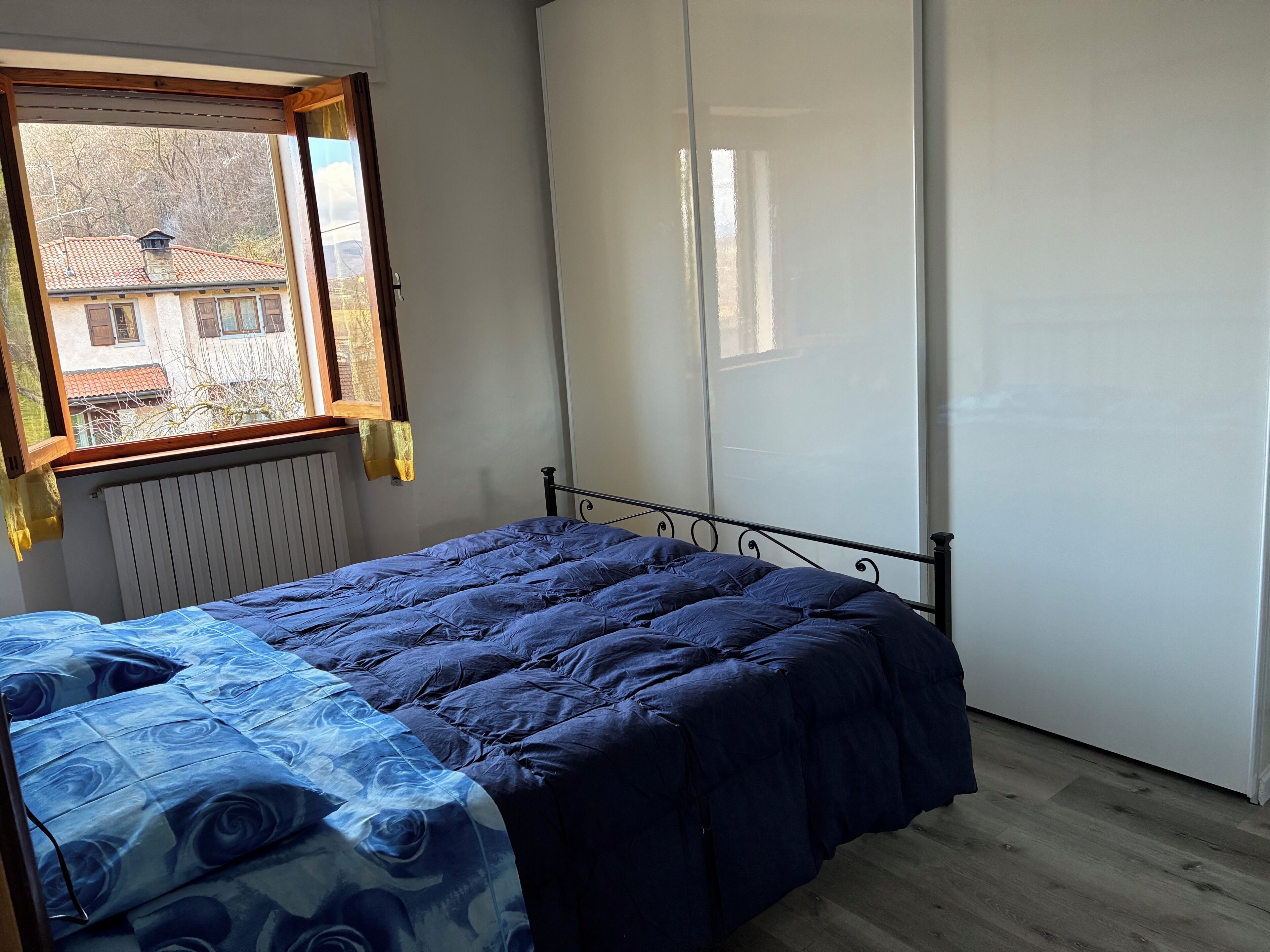 A bedroom with a bed, a radiator, a window, and a wardrobe.